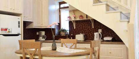 A kitchen with a dining table, chairs, a coffee maker, and a staircase.