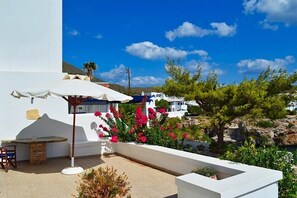 A terrace with a table and chairs, a white umbrella, and red flowers. - Maryianni Apartments (Kithira)