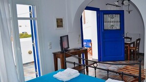 A room with a bed, a television on a wooden table, a blue door, and a view of the outside. - Maryianni Apartments (Kithira)