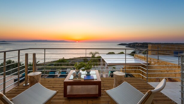 A wooden deck with lounge chairs and a table, overlooking a sunset over a body of water. - Yellow Dream Villas (Chania)