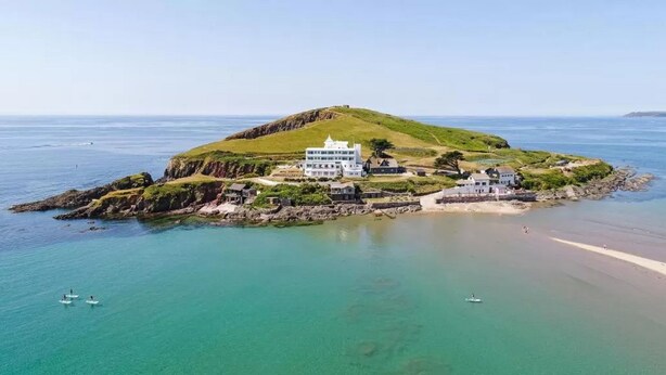A coastal property with multiple buildings, including a large white structure and smaller houses, surrounded by clear blue waters and a sandy beach.