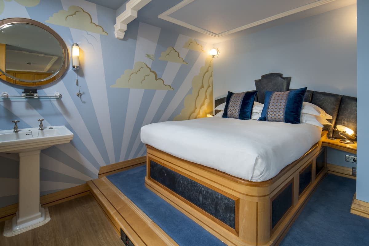 A bedroom with a bed, bedside table, lamp, and a wall-mounted mirror.