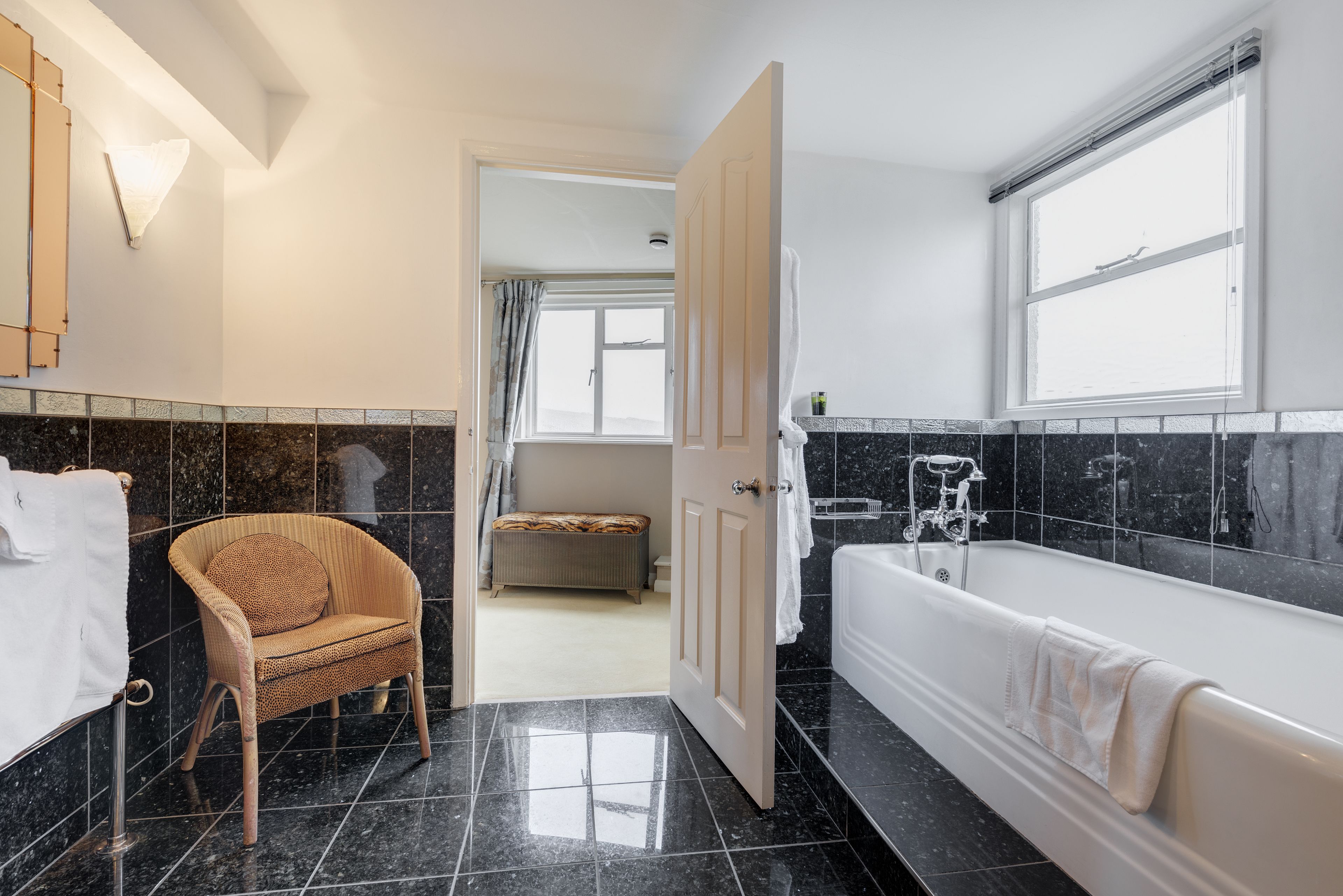 Un bagno moderno con una vasca da bagno grande, una poltrona in vimini e vista sulla stanza comunicante.