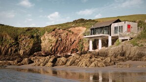 A coastal house with a balcony overlooking the beach and cliffs.