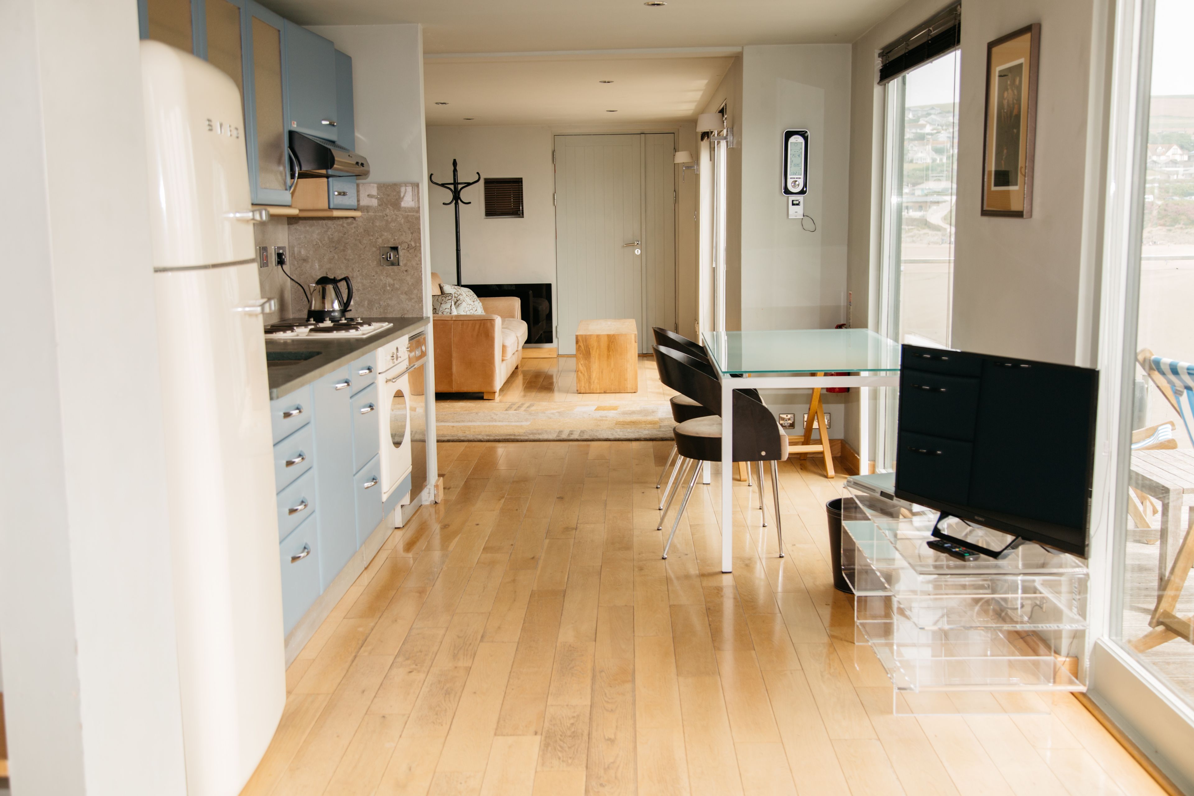 A modern kitchen with light blue cabinets, a wooden floor, and a dining area with a glass table and chairs.