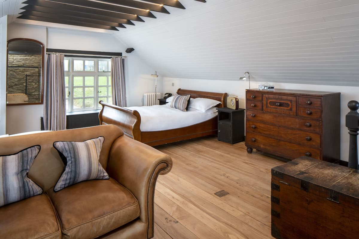 A bedroom with a bed, wooden dresser, and a leather sofa.