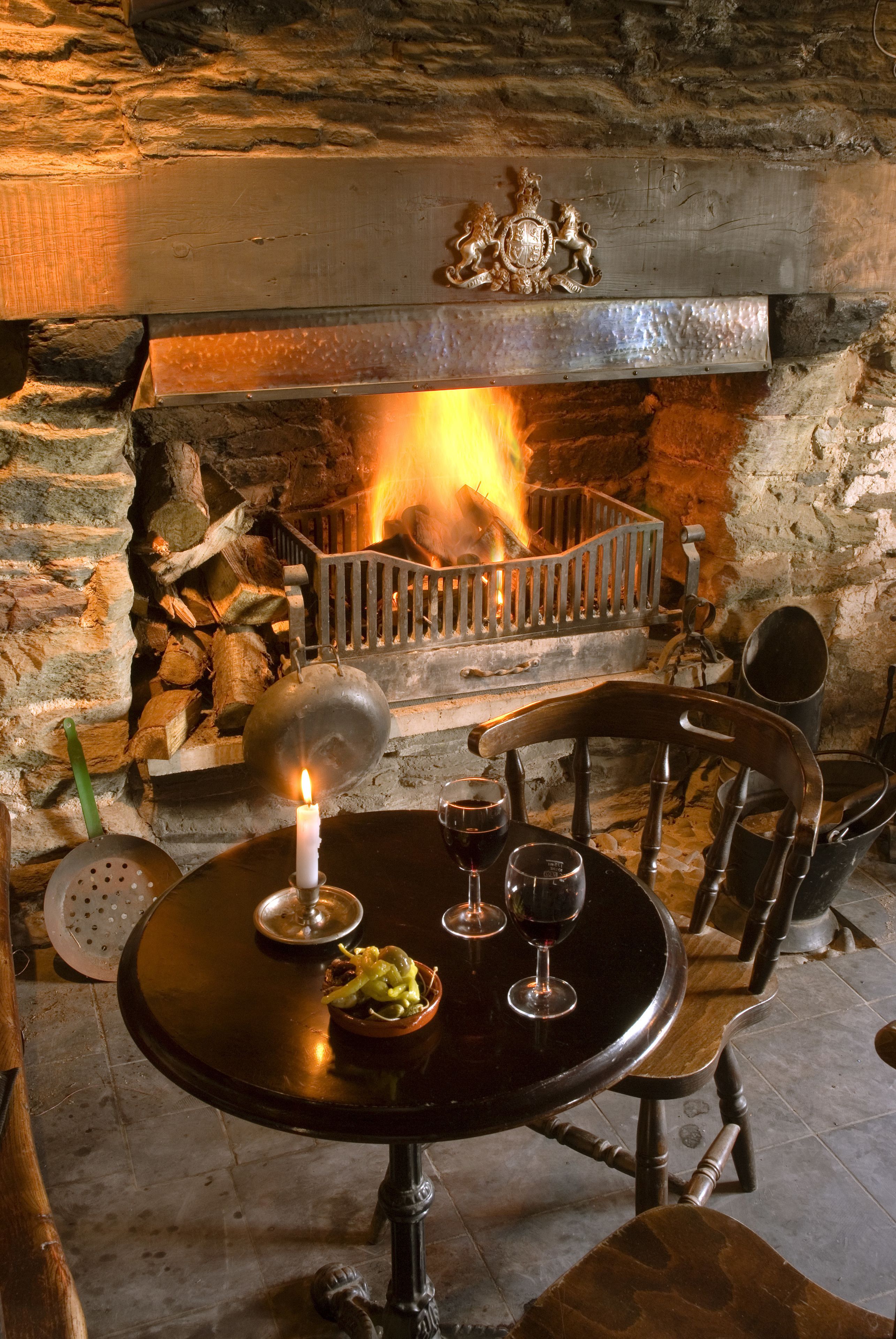 Une cheminée en pierre avec un feu, une table avec une bougie et un bol de nourriture.