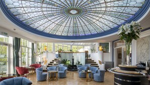 A spacious lobby with a high ceiling and a central fountain, surrounded by blue armchairs and a bar area.