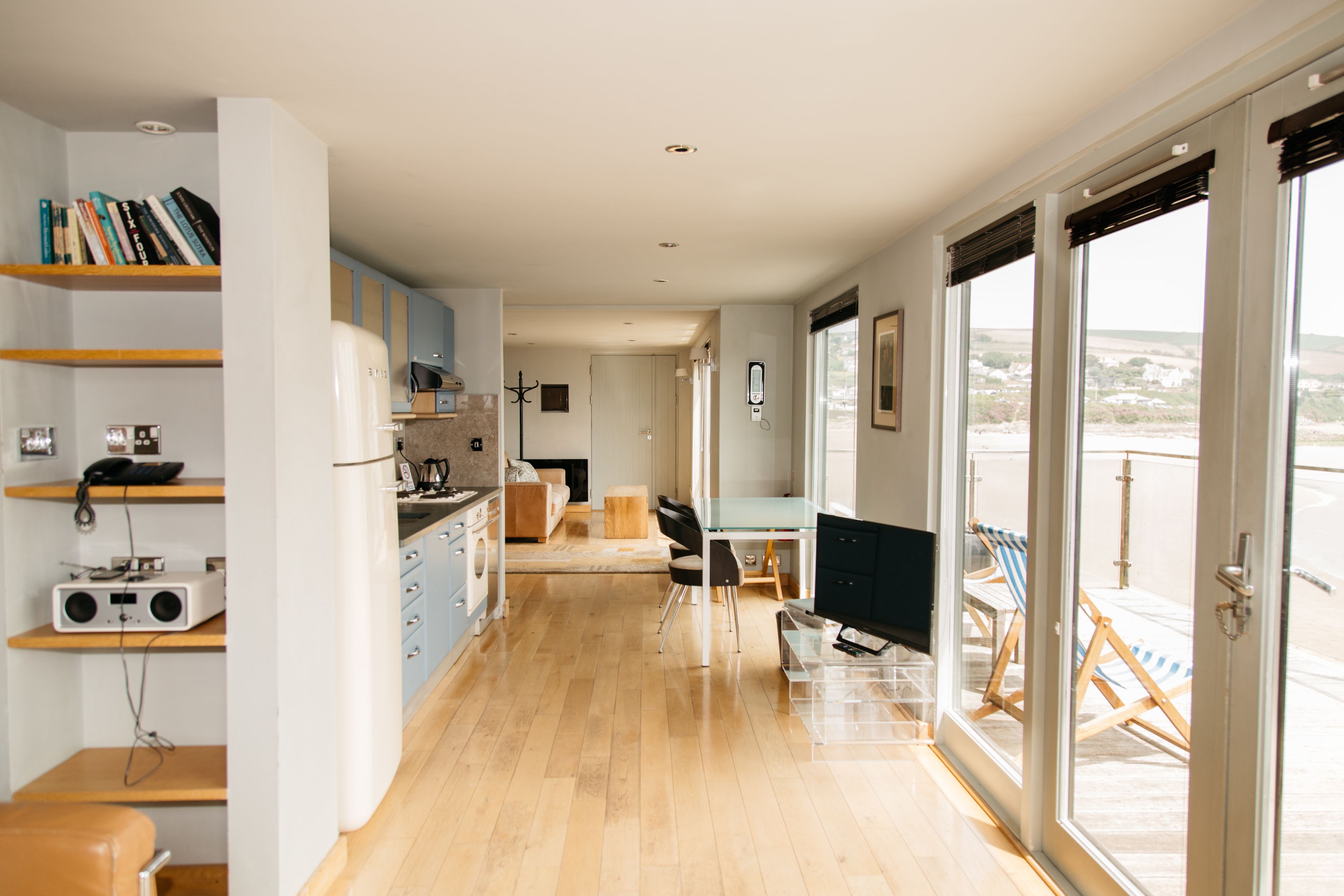 Una cocina moderna con armarios de madera, un comedor con mesa de vidrio y vistas a través de amplios ventanales correderas.