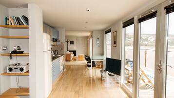 Una cocina moderna con armarios de madera, un comedor con mesa de vidrio y vistas a través de amplios ventanales correderas.