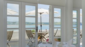 A dining area with a table set for two, overlooking a scenic view of the sea and hills.