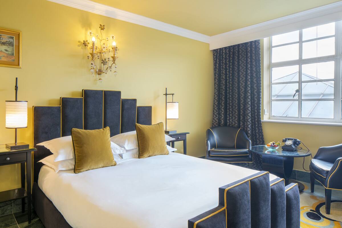 A hotel room with a large bed, two bedside tables, a desk, a chair, and a window with a view.