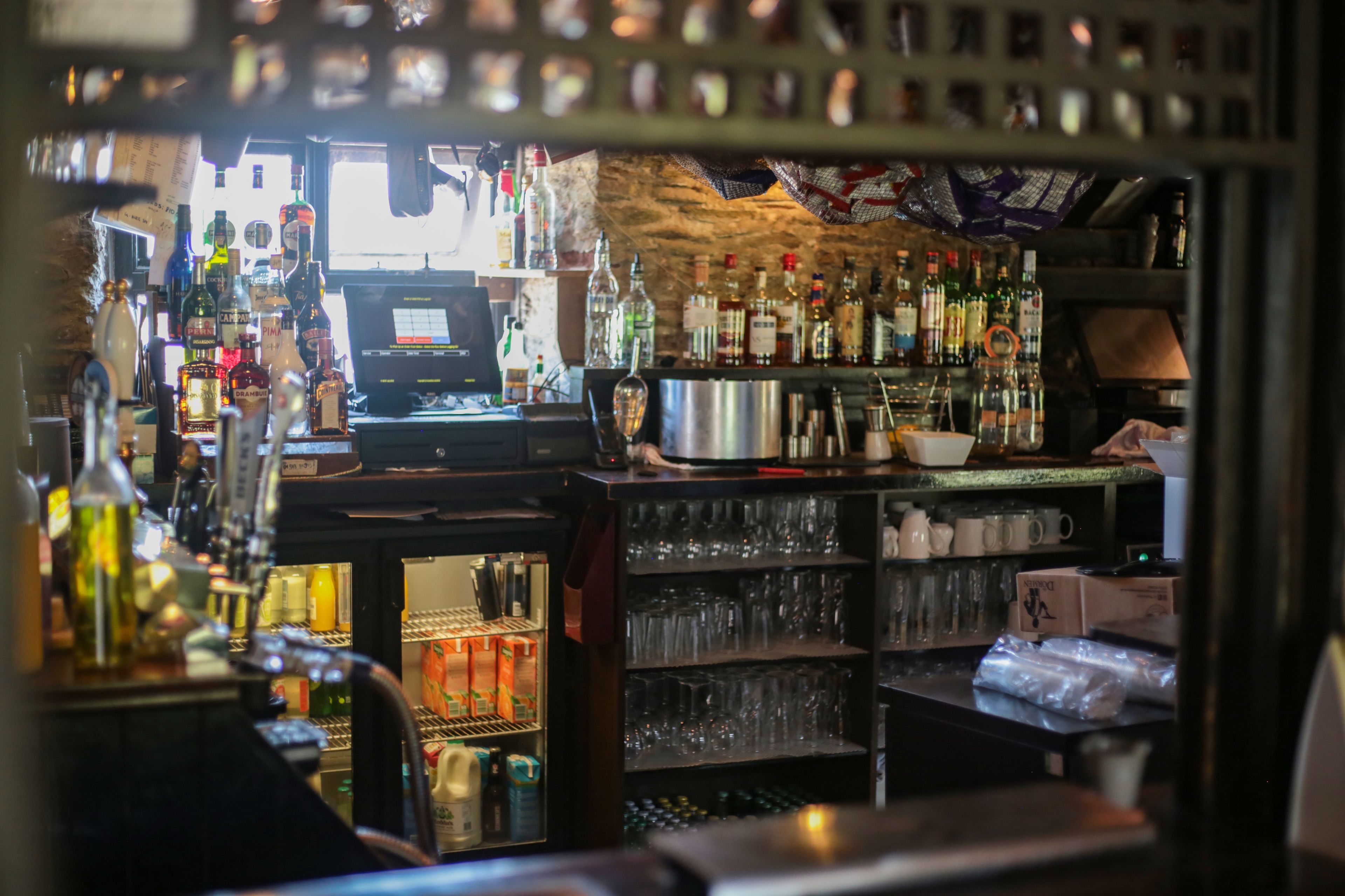 Una zona de bar con estantes llenos de botellas, vasos y una caja registradora.