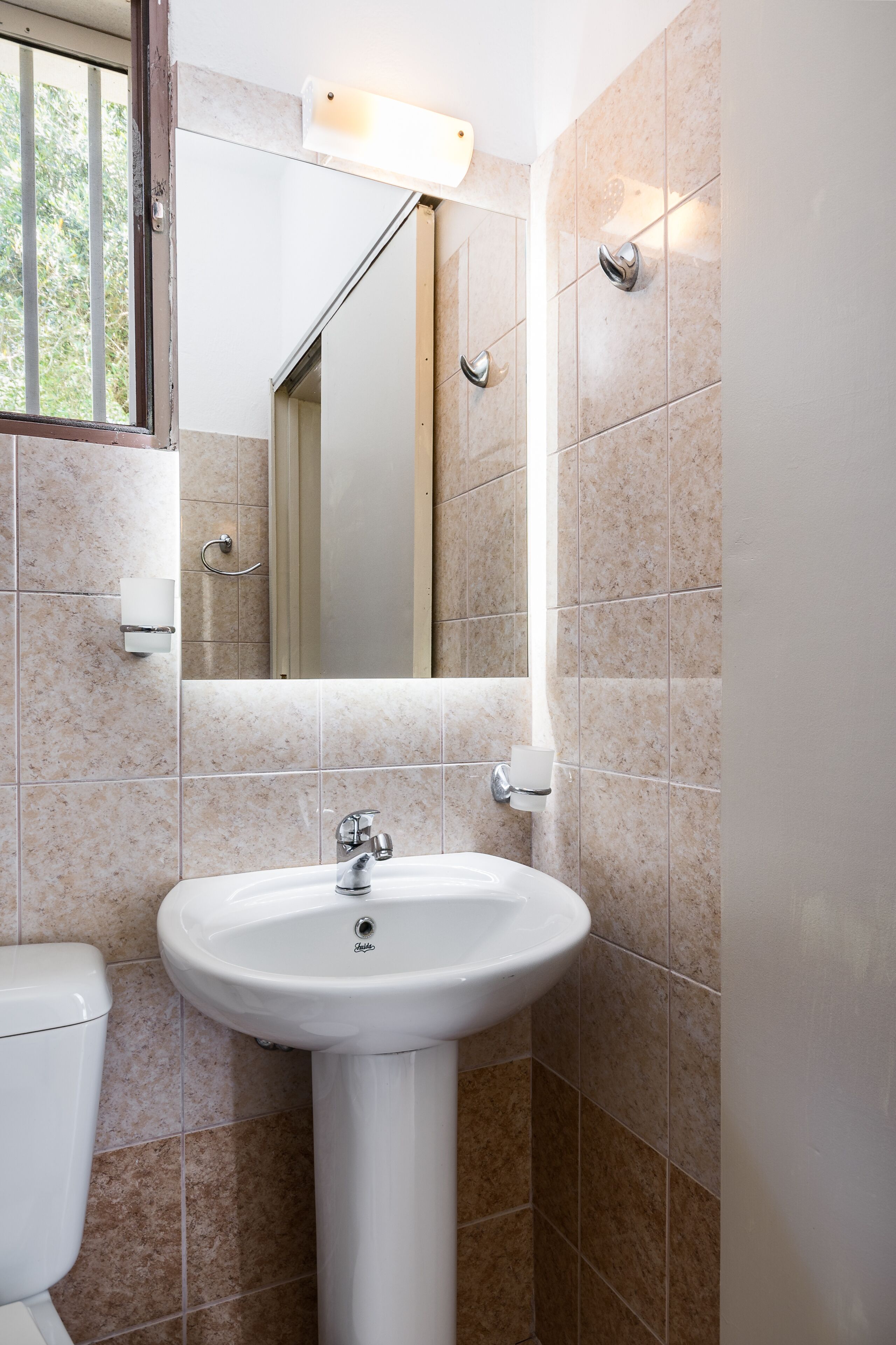 Een badkamer met een wit wastafel, een spiegel en beige tegels.