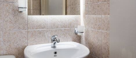 Een badkamer met een wit wastafel, een spiegel en beige tegels.