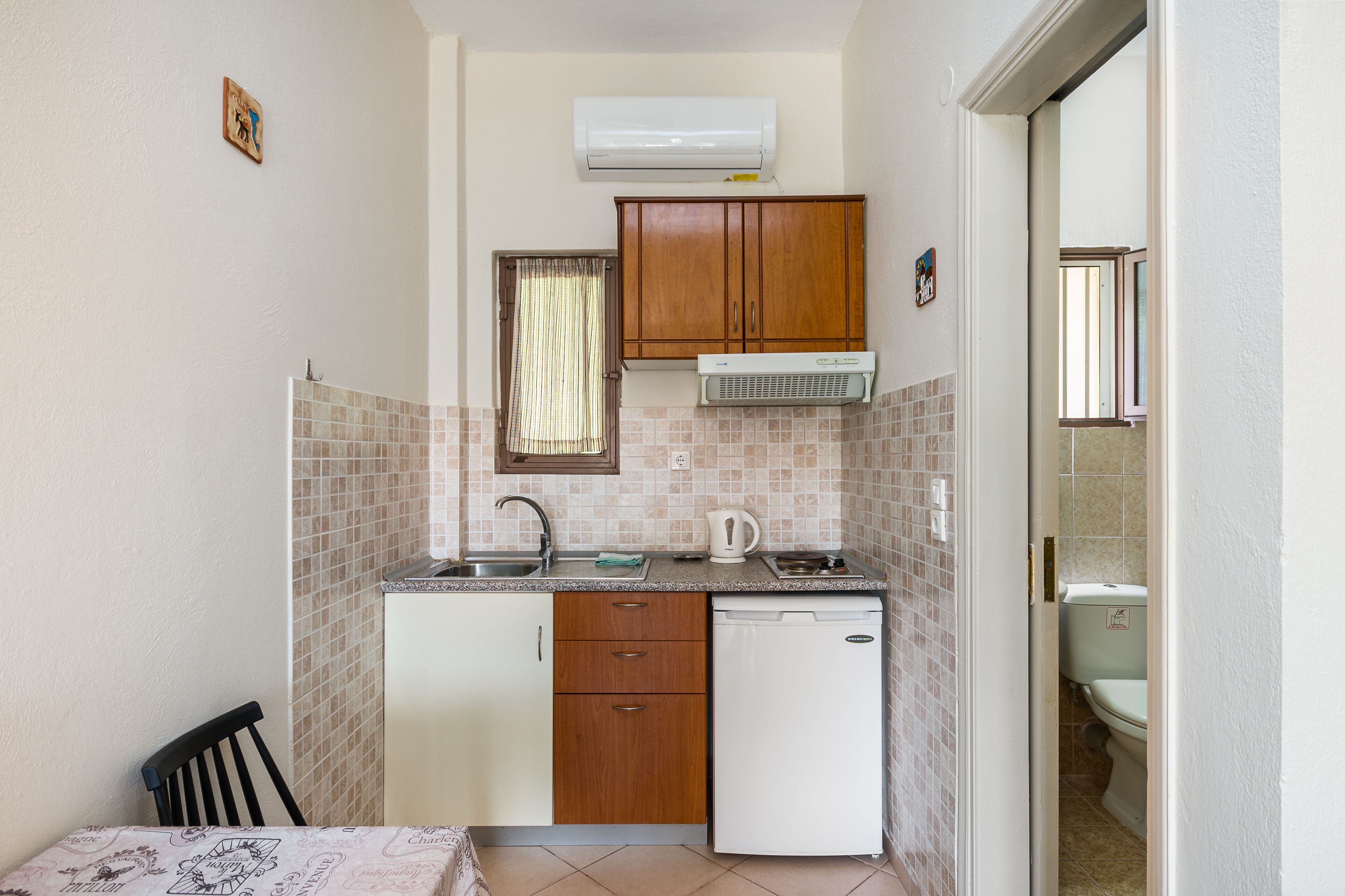 A compact kitchen with a dishwasher, a sink, and a window with curtains.
