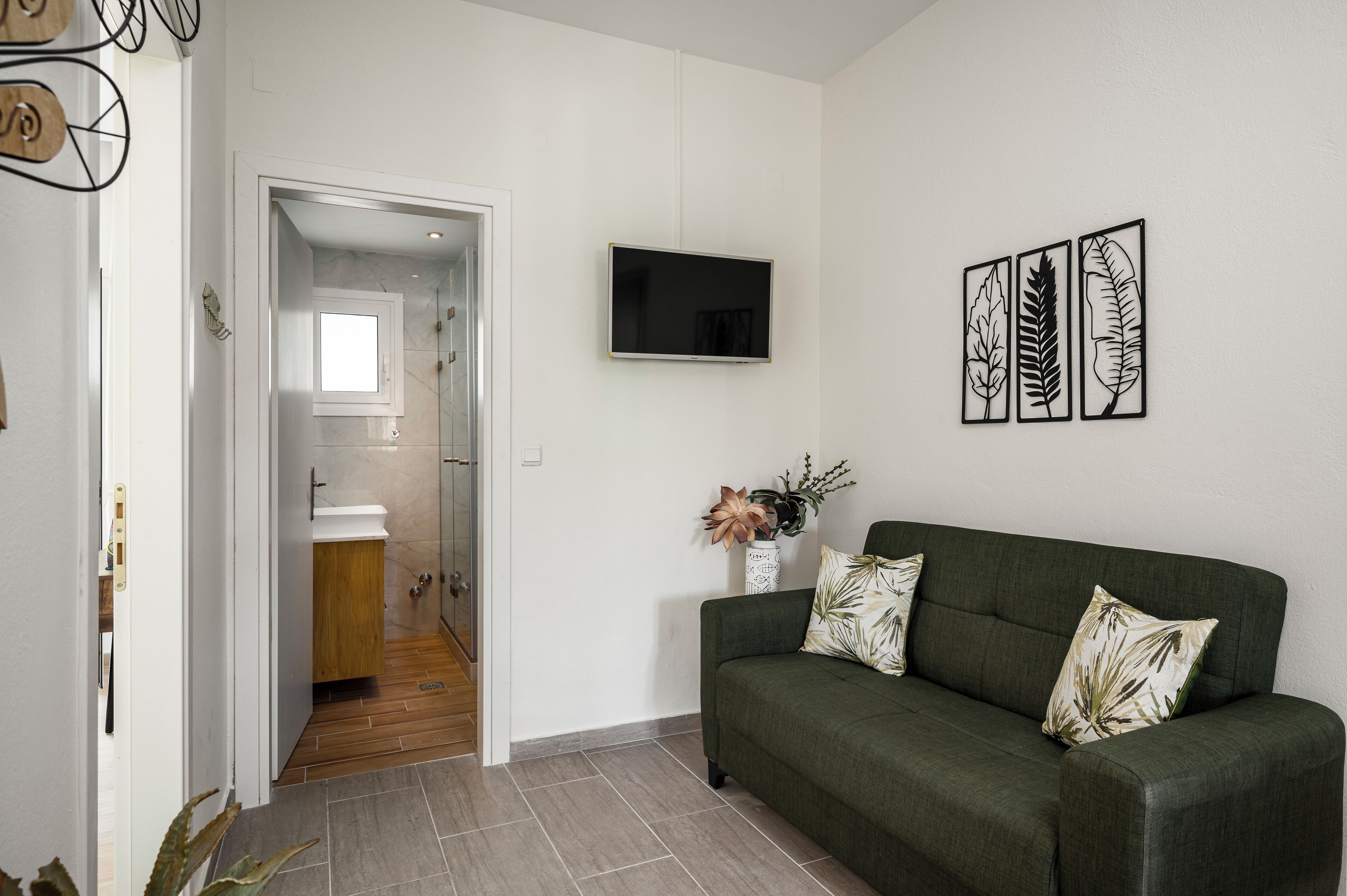 A modern living room with a green sofa, a flat-screen TV, and three leaf-patterned wall art pieces.