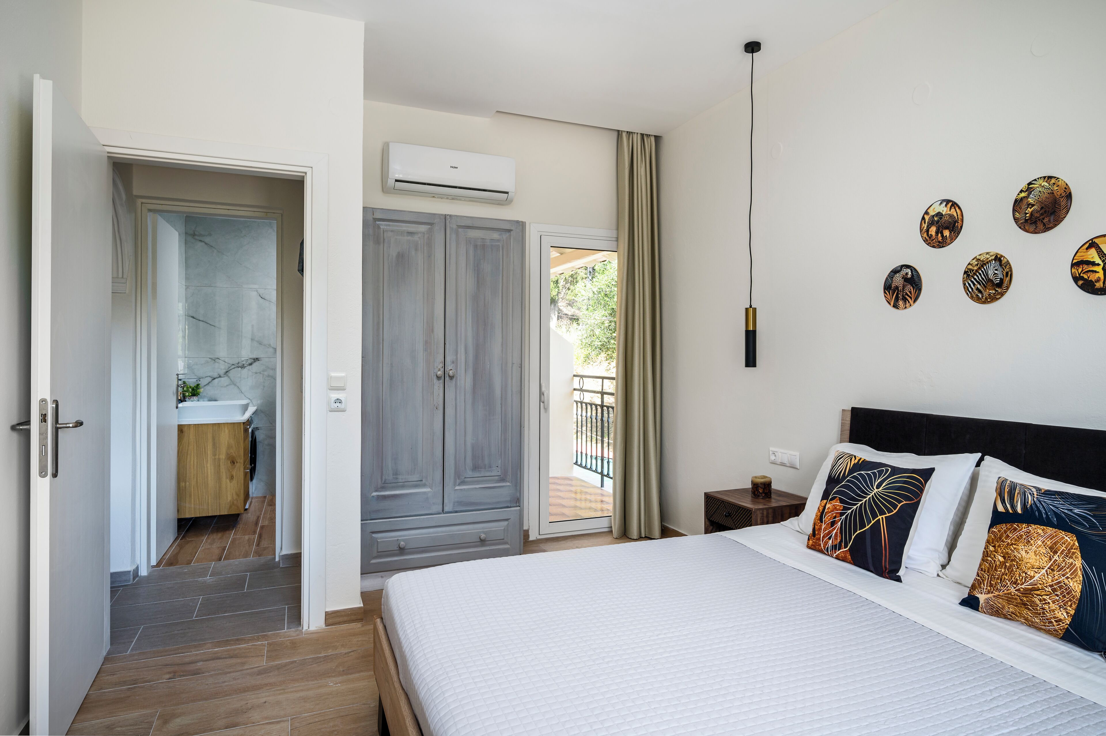 A bedroom with a bed, a nightstand, a dresser, a bathroom with a sink, and a balcony.