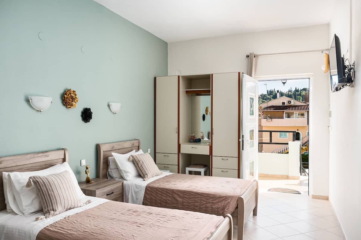 A bedroom with two beds, a wardrobe, and a balcony with a view of buildings.