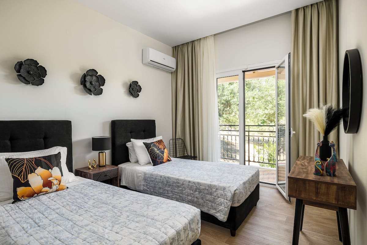 A hotel room with two beds, a balcony, an air conditioning unit, and a decorative vase.