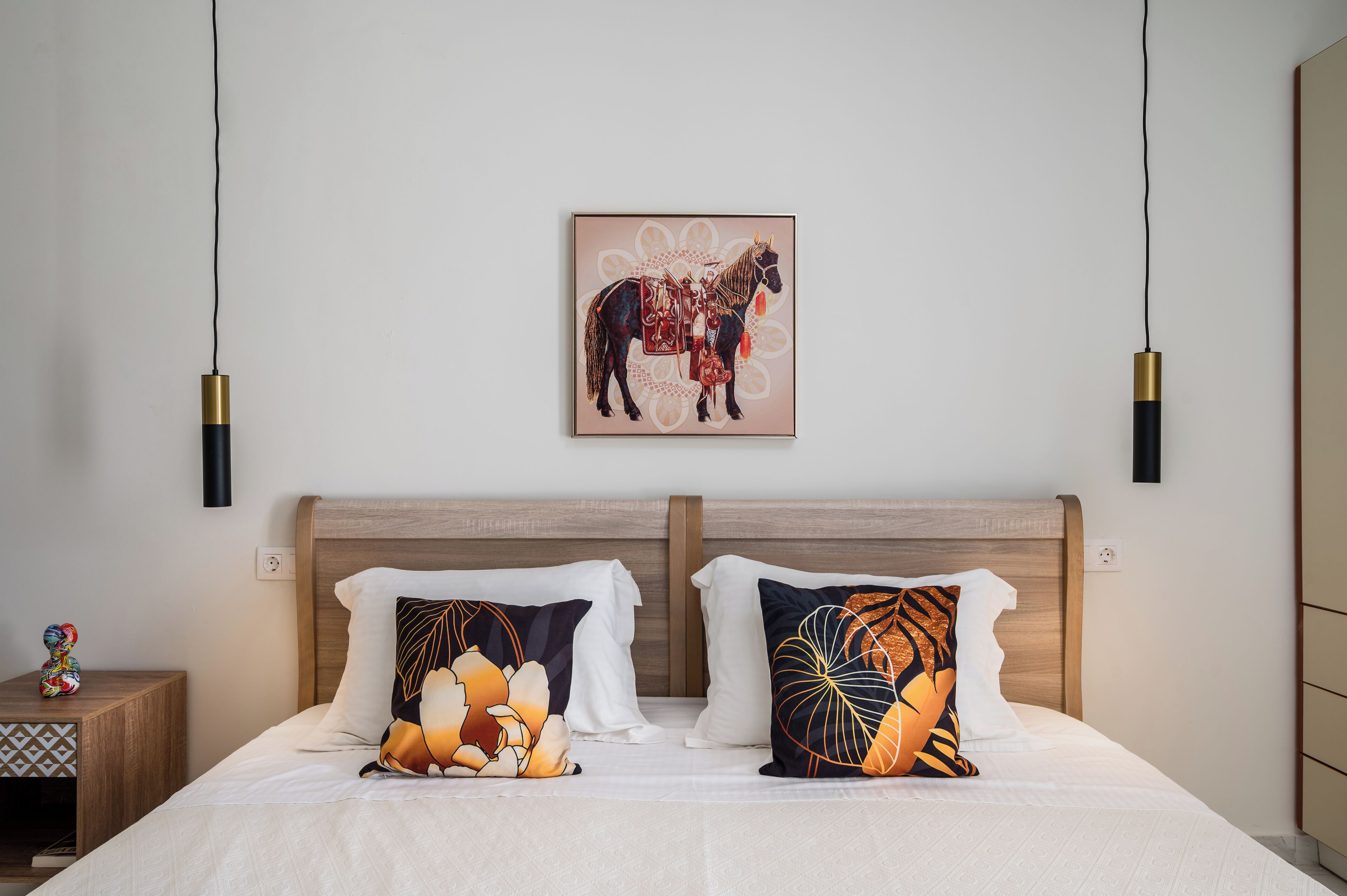 A neatly made bed with two pillows, a wall-mounted artwork of a horse, and a bedside table with a decorative item.