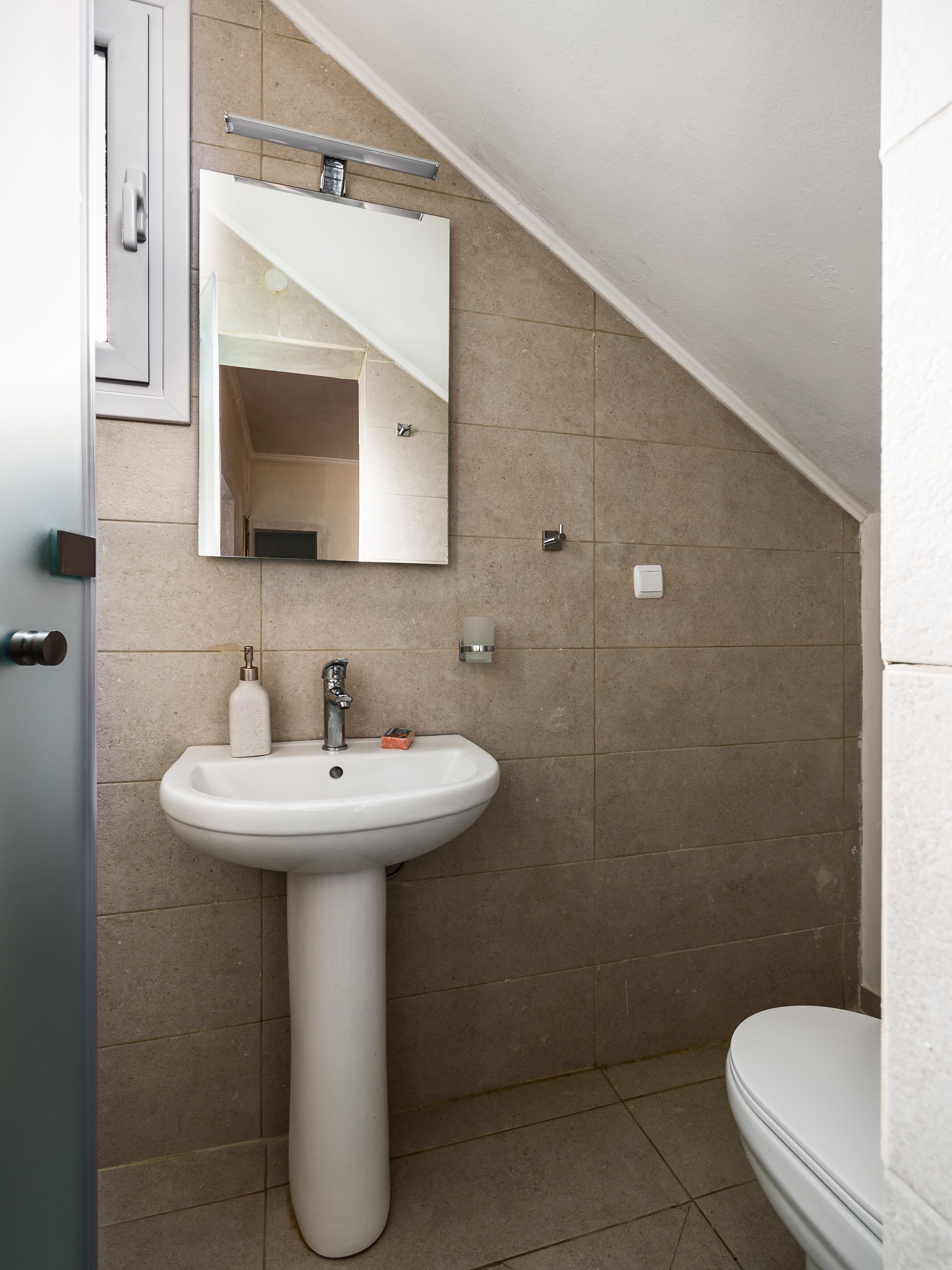 A bathroom with a pedestal sink, a mirror, and a toilet.