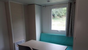 Une petite pièce avec une seule table et deux chaises, une fenêtre avec des rideaux et un banc intégré.