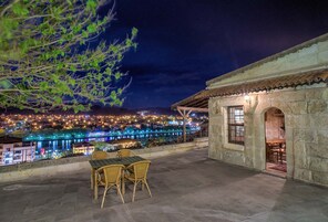 Un patio al aire libre con una mesa y sillas, con vista a un paisaje urbano nocturno.