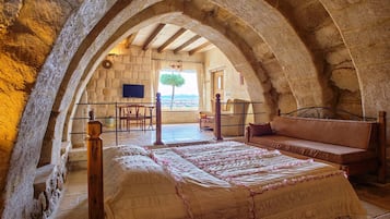 Un dormitorio con un arco de piedra, una cama con colcha estampada, un banco de madera y vistas al exterior.