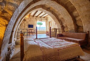 A bedroom with a stone archway, a bed with a patterned bedspread, a wooden bench, and a view of the outdoors.