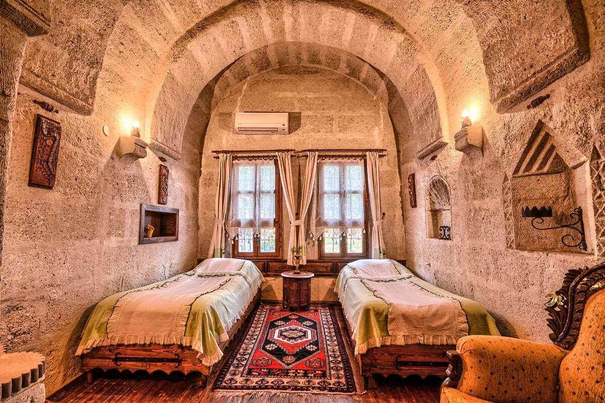A room with two beds, a rug, and stone walls.