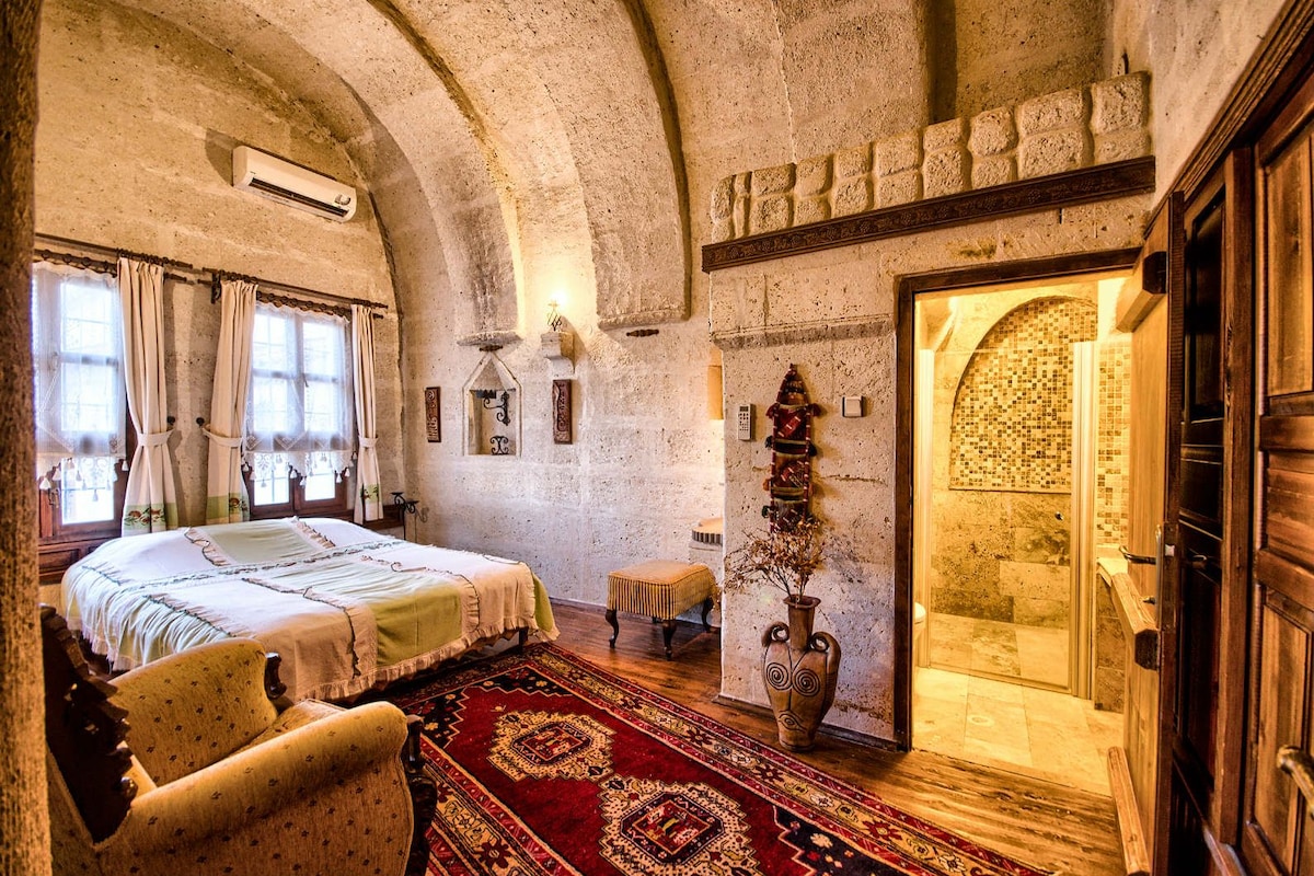 Una habitación con cama, una mesita, un jarrón decorativo y zona de ducha.