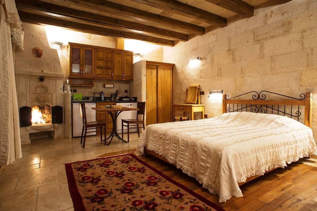 Um quarto aconchegante com cama, escrivaninha, lareira e cozinha.