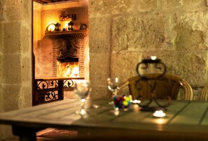 Una mesa con una copa, una vela y objetos decorativos frente a una chimenea con un fondo de pared de piedra.