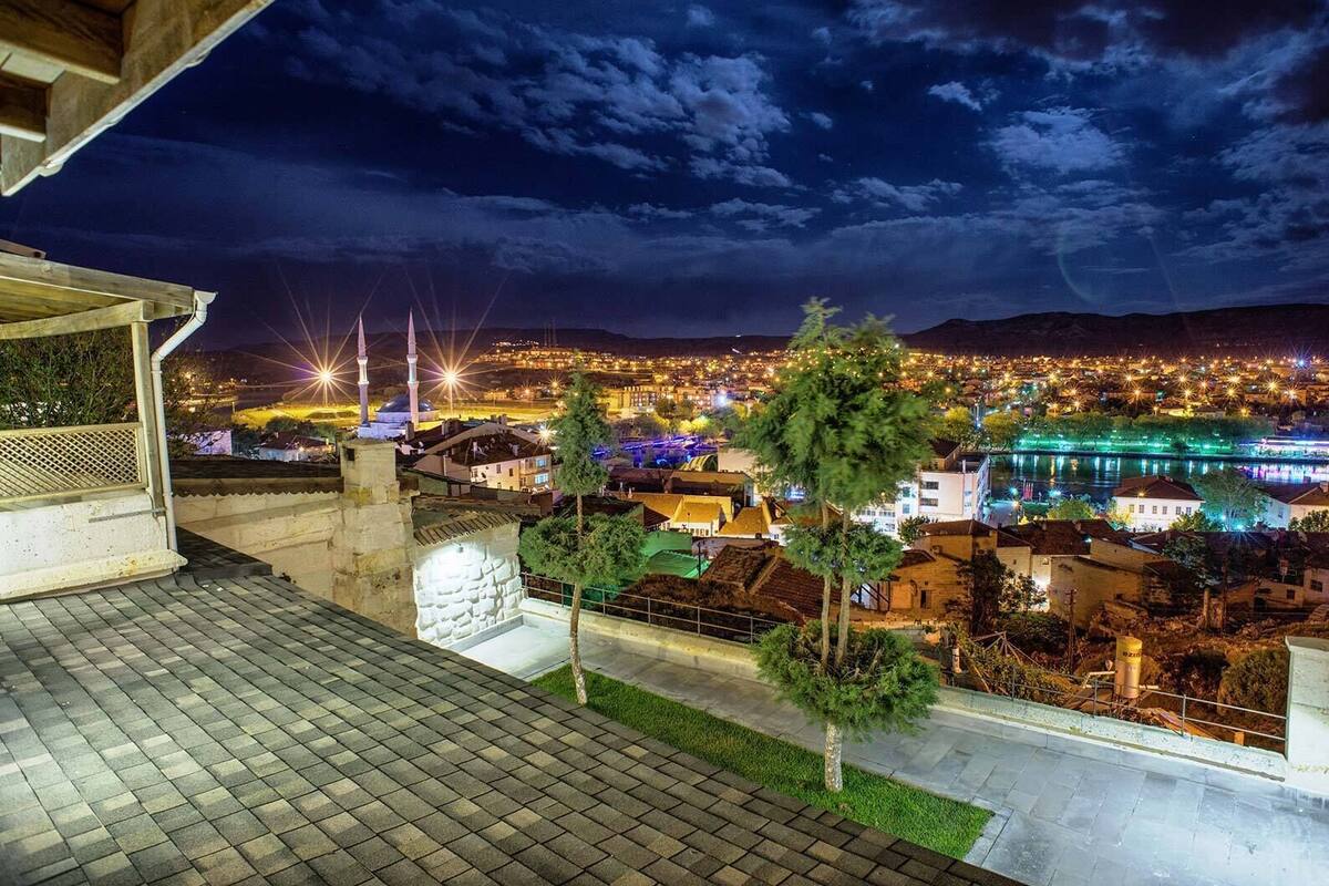Vista noturna de um horizonte urbano com edifícios iluminados, uma mesquita com minaretes e um rio refletindo luzes.