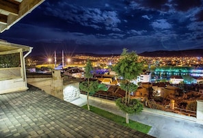 A nighttime view of a cityscape with illuminated buildings, a mosque with minarets, and a river reflecting lights. - Avanos Evi (Avanos)