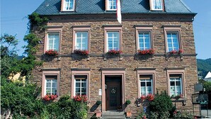 A stone building with a symmetrical facade, multiple windows, and flower boxes. - Weinhof Gassen (Kröv)
