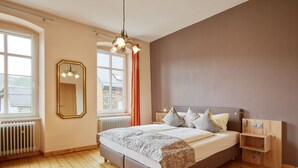 A bedroom with a large bed, a mirror, a radiator, and a window with curtains. - Weinhof Gassen (Kröv)