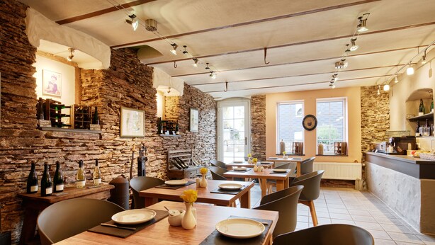 A restaurant with stone walls, wooden tables, and chairs. There are wine bottles on shelves and a counter with a menu. - Weinhof Gassen (Kröv)