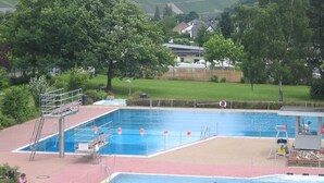 A swimming pool with diving boards, surrounded by trees and a hilly landscape in the background. - Weinhof Gassen (Kröv)
