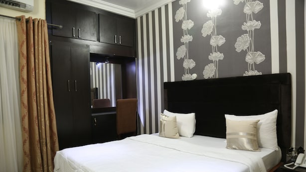 A hotel room with a large bed, a wardrobe, a desk with a telephone, and a mirror. - Nelseno Hotel (Abuja)