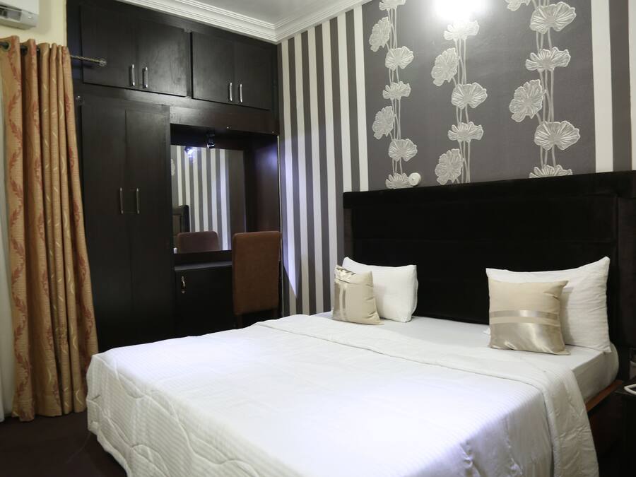 Una habitación de hotel con una cama grande, un armario, un escritorio con teléfono y un espejo.