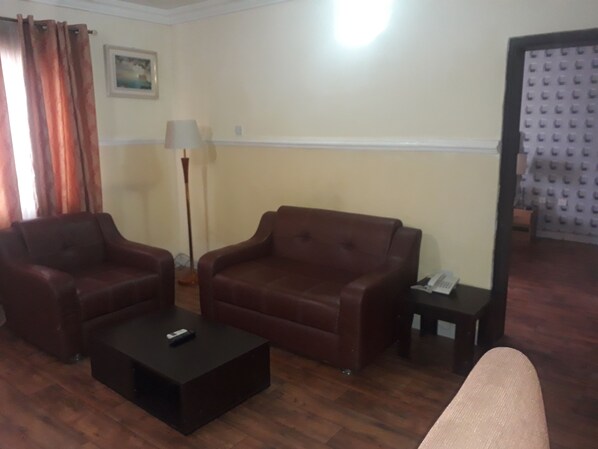 Una sala de estar con un sofá marrón, un sillón más pequeño, una mesa de centro y una lámpara.