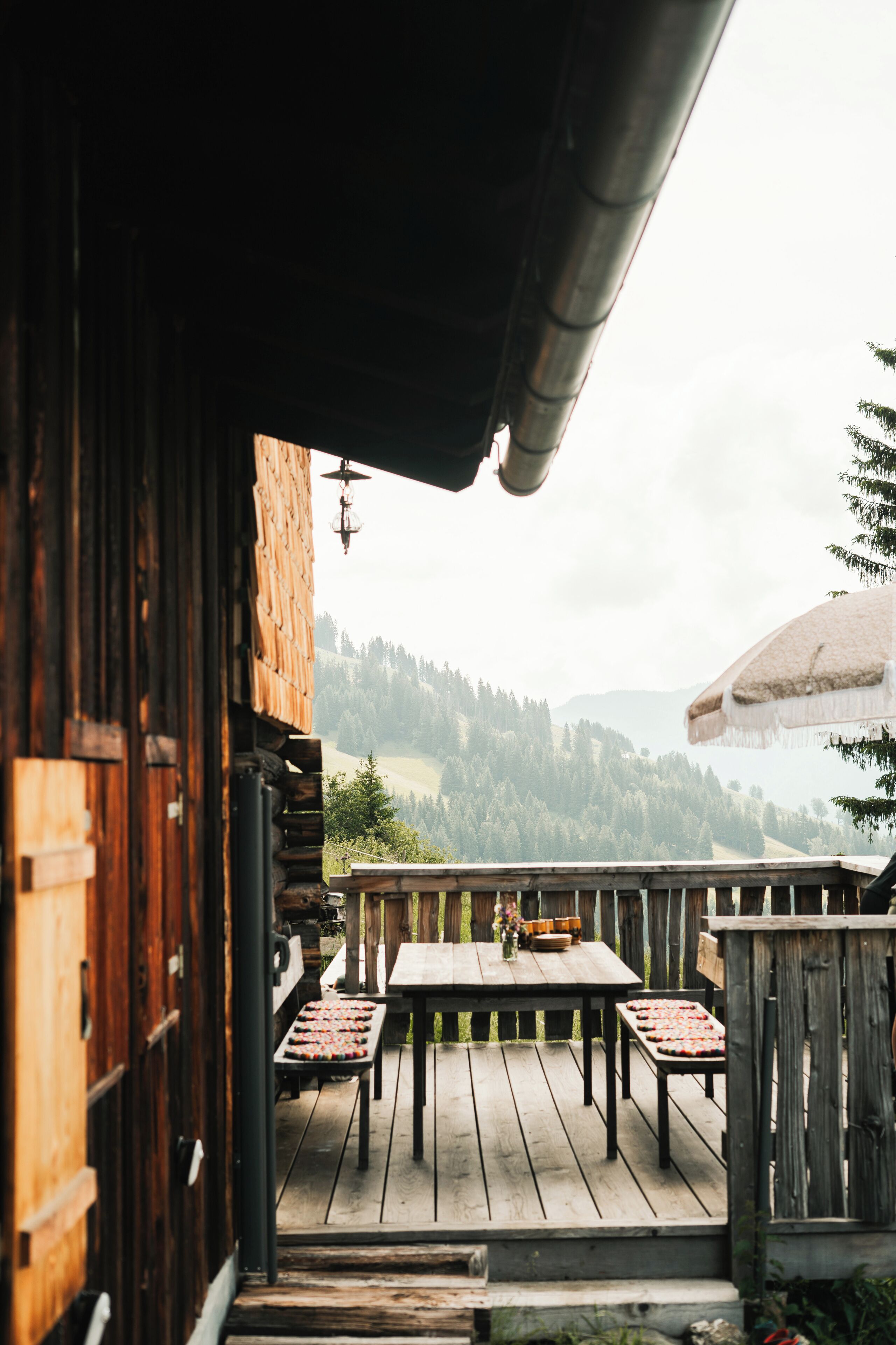 Terraza de madera con mesa y sillas, con vistas a un paisaje montañoso.