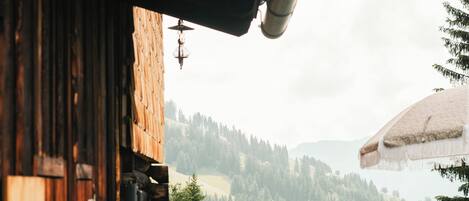 Terraza de madera con mesa y sillas, con vistas a un paisaje montañoso.