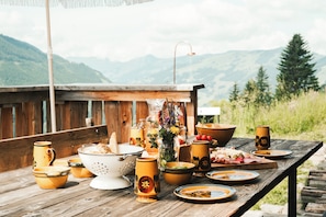 A wooden table set with various dishes and utensils, a vase with flowers, and a view of mountains in the background. - Hotel Glemmtalerhof (Saalbach-Hinterglemm)