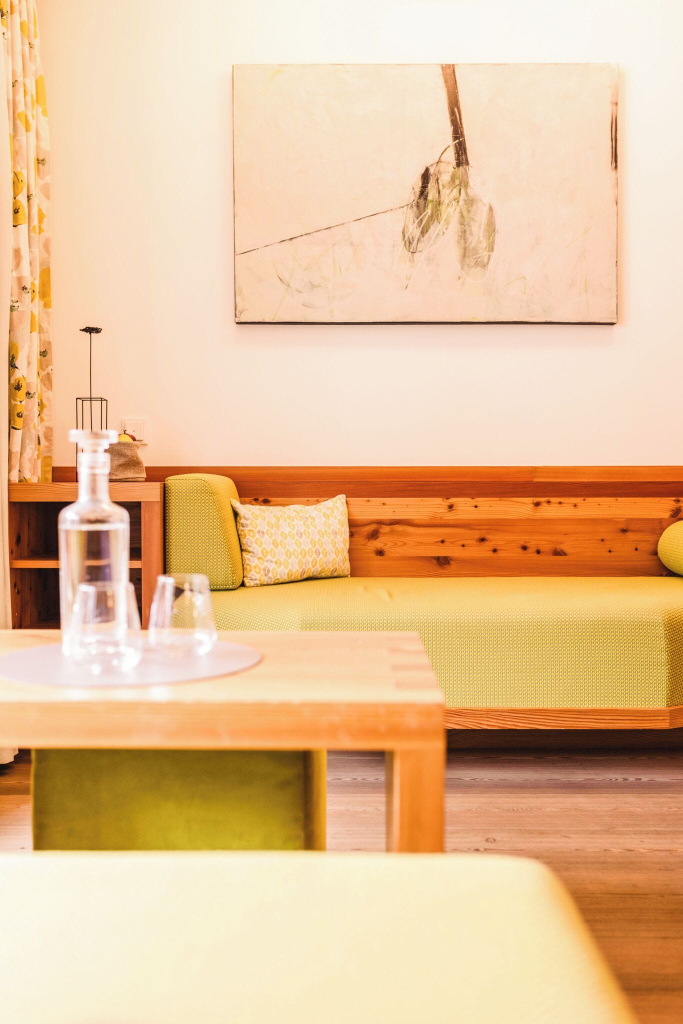 A cozy room with a wooden sofa, a table with glasses and a bottle, and a painting on the wall.