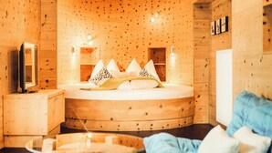 Una habitación de cabaña de madera con una cama redonda, mesitas de noche, un televisor y una mesa de cristal.