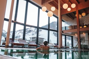 Una piscina interior amb grans finestres, bigues de fusta i gandules.