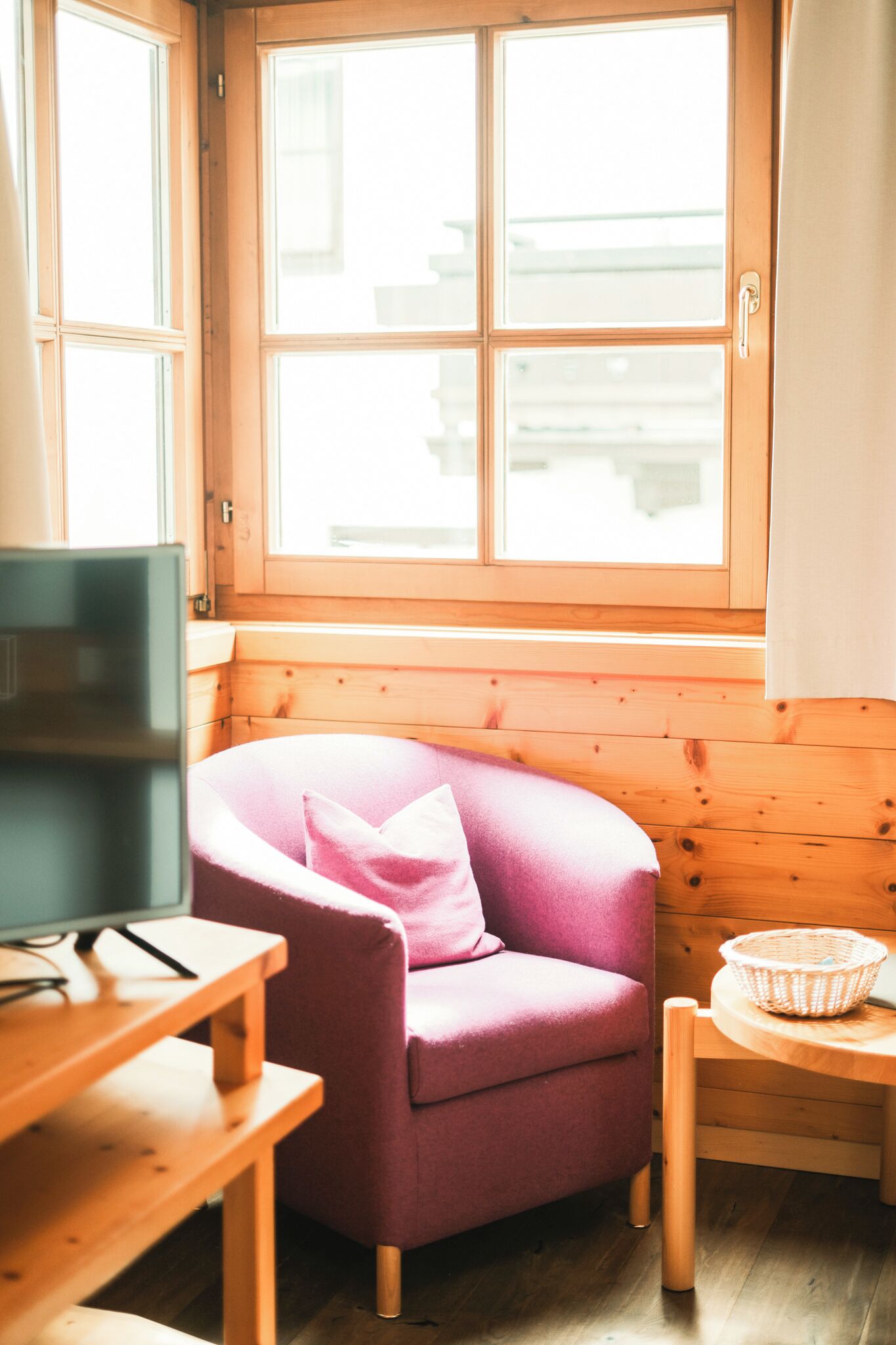 A room with a wooden interior, a purple armchair, a small wooden table, and a window with a view.